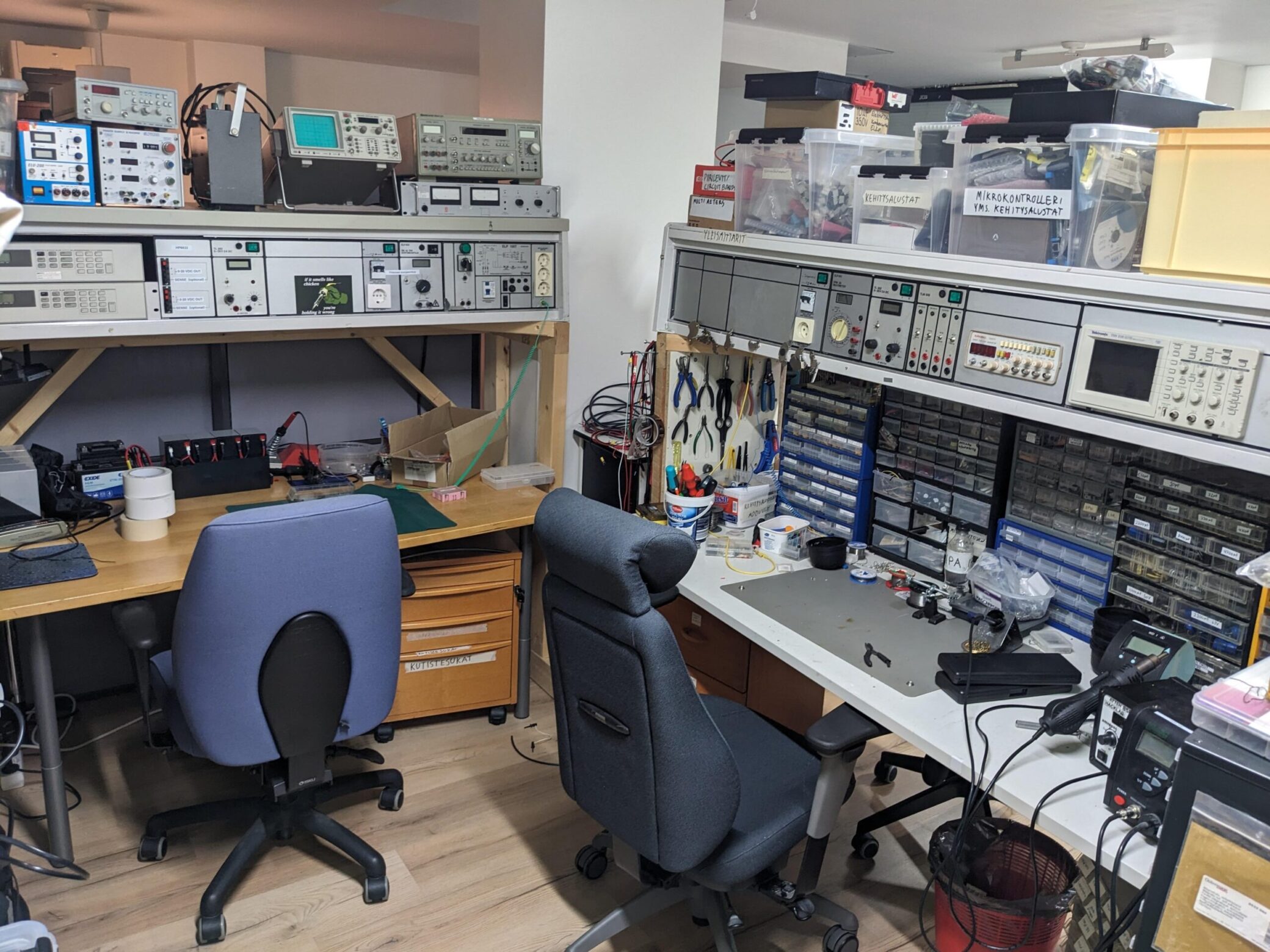 A corner with electronics workbenches filled with tools and hardware