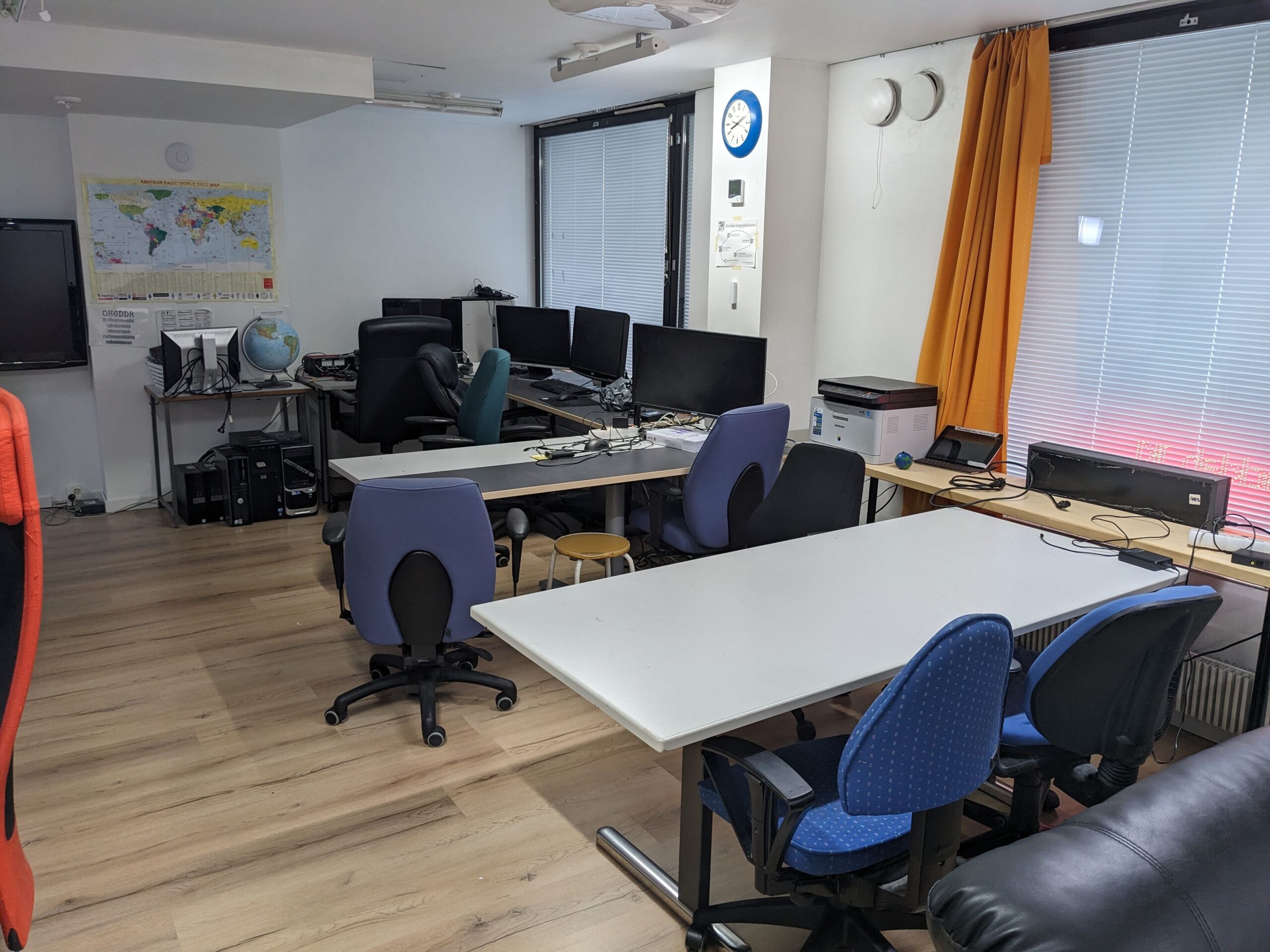 Several desks and desk chairs, some desks have computers and monitors on them. A world map hangs on the far wall